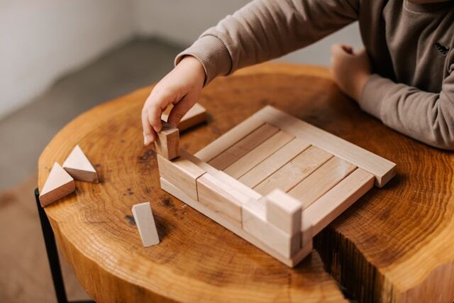 Woman’s hands assembling a wooden puzzle on a table in natural light, reflecting quiet focus and the beginning of inner clarity.